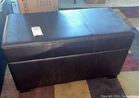 Closed view of black rectangular storage bench with faux leather upholstery showing rectangular stitched design.