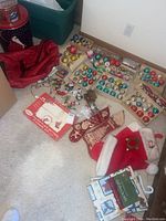 Wide view of lot showing various boxes of vintage glass ornaments in multiple colors, red Santa hats, embroidered Christmas stockings, packaged holiday place settings, and other loose festive decorations.
