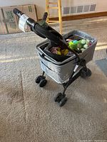 Side view of gray dog stroller holding multiple dog toys inside, placed on carpeted floor.