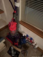 Dyson vacuum upright cleaner with attachments and cleaning products placed on the floor near a window.