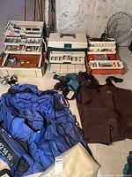Photo showing blue float tube, brown fishing vest, two tackle boxes, and base of fishing rods leaning on the wall.