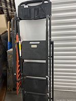 Front view of foldable HB Tower step stool with four textured steps and attached fabric tool pouch at top handle.