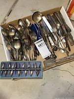 Photo showing an assortment of tarnished silver plate silverware including forks, spoons, knives, and serving pieces along with a boxed set of 12 metal corn cob holders.