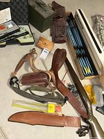 Overview of sporting goods including arrows in quiver, leather belts and sheaths, wooden rifle stock, cleaning rods, and ammo box.