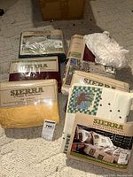 Photo of multiple bedding sheet packages from Sierra Home Collections on carpeted floor. Sheets in various colors and patterns shown with packaging labels.