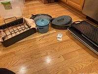 Wide view of all pots, pans, baking trays, and racks on wood floor, showing condition and assortment.