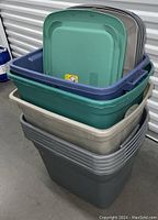 Several stacked plastic storage totes of various colors with multiple plastic lids nested inside.