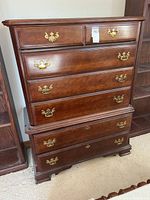 Front view of tall dark wood dresser showing brass hardware and drawer arrangement