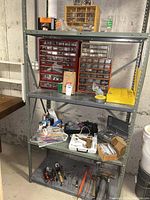 Wide view showing metal shelving with compartment organizers full of screws, bolts, and crafting tools including glue tool and various hand tools on lower shelf.