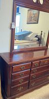 Dresser top with attached large mirror showing reflection of room. Mirror frame has ornate carved finial at top center.