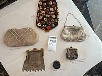 Top-down view of all five vintage purses including a pearl clutch, embroidered textile pouch, mesh purse, lace frame purse, and coin purse on white surface