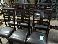Front view of six Parsons style chairs with dark wood frames and black faux leather seats grouped together.