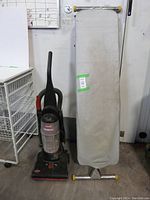 Bissell PowerTrack vacuum cleaner and ironing board standing side by side, shows vacuum front and ironing board front cover.