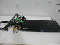 Photo of LG Blu-ray player showing front panel and attached cords on a white surface.