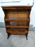 Front view of wooden bookcase hutch showing three shelves and scalloped top edge.