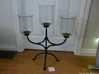 Front view of the triple candle holder showing the metal frame and three clear glass chimneys.
