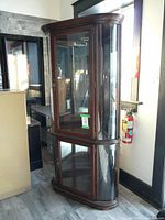 Full view of wood and glass corner curio cabinet showing upper and lower glass door sections, curved glass sides, and wood frame.