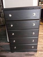 Front view of a dark colored dresser with five drawers and metal round handles