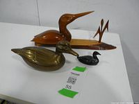 Full view of all three duck sculptures displayed on a white table, showing size and material differences.