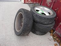 Four Zenna Sport Line tires stacked and leaning against a rusted red metal door on a concrete ground. Shows overall condition of tires and rims with dirt and wear visible.