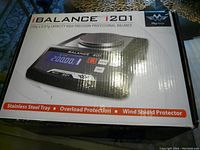 Box showing the product branding and features including 700g x 0.01g capacity, stainless steel tray, overload protection, and wind shield protector.