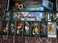 Top open view of tacklebox showing compartments with assorted vintage lures and tackle inside.