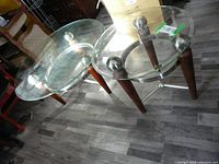 Photo showing both coffee table and side table with glass tops, wood legs with metal caps, and visible metal frame underneath glass on the coffee table for support.