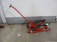 Full view of red hydraulic motorcycle jack showing frame, handle, and lifting platform.