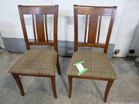 Pair of wooden chairs with beige fabric seats and vertical slat backs, shown side by side on concrete floor.