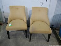 Front view of two light butterscotch fabric occasional chairs side by side with hobnail tack detail on edges and one button tuft on backrest. Legs are dark wood.