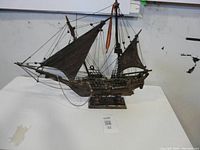 Full view of wooden pirate ship model showing three masts, brown fabric sails, and wooden base.
