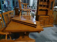 Photo showing the pine rectangular dining table with two removable leaves stacked on top, and five wooden chairs surrounding the table; includes two armchairs and four side chairs visible.