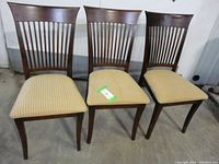 Full front view of the three wooden side chairs showing the tall slatted backs and striped fabric seats.