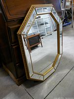 Full view of the octagonal wall mirror leaning against a wooden furniture piece, showing the overall shape and size in a storage or warehouse area.