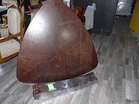 Photo of dark wood triangular table top with wood grain and signs of wear, placed against a wall