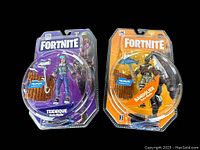 Front view of Teknique and Bandolier Fortnite action figures in sealed blister packaging showing figures and accessories.