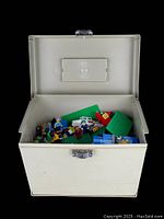Open cream-colored vintage file folder case with loose Lego bricks, baseplates, and minifigures inside.