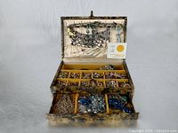 View of open Mele case showing collection of vintage jewelry arranged in cushioned compartments including necklaces, earrings, pins, and bracelets.