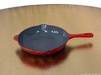 Le Creuset cast iron skillet grill pan with red-orange exterior and gray enamel interior shown from an angle.