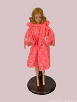 Front view of vintage 1960s Mattel Barbie Midge doll standing on black stand, wearing pink sheer floral lace coat with fur trim on cuffs and collar.