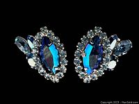 Close-up photo of one pair of blue iridescent clip on earrings with clear rhinestones surrounding and accenting stones