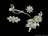 Five vintage rhinestone brooches displayed on a black background, showing both the detailed front view including one with a faux pearl and a floral motif cluster.