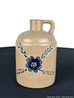 Front view of a beige vintage stoneware jug with a blue floral and leaf design and crackled glaze on a black background.