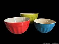 Set of three nesting ceramic bowls shown individually and nested, highlighting large green, medium red, and small blue bowls with textured exterior and cream interior.