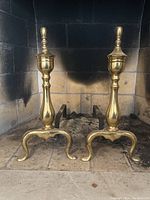 Pair of classic solid brass fireplace andirons inside a brick fireplace, staged in empty state.