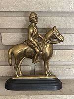 Front and side views of a solid brass figure of a man on a horse, mounted on a black wooden base, showing detail and condition.