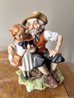 Full view of the figurine showing both the girl and the seated elderly man on a tree stump base.