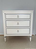 Front view of the 3 drawer painted nightstand showing drawer pulls and minor chip on top drawer.