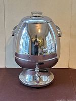 Front view of a shiny stainless steel electric coffee percolator samovar with pedestal base, spigot, and glass knob lid.