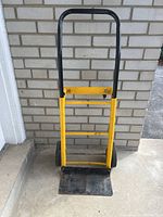 Front view of a yellow and black metal dolly with removable handle, showing the base plate and wheels.